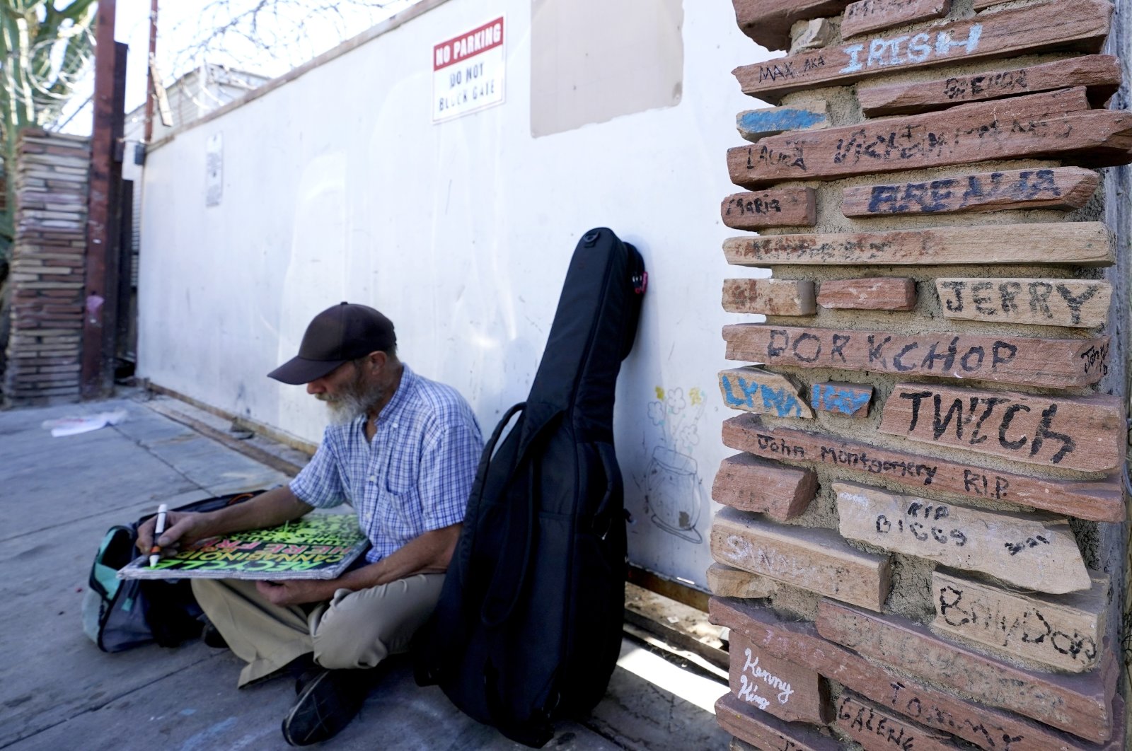 A homeless man works on a sign as he sits next a monument to homeless people who have died Phoenix, Arizona, U.S., April 27, 2022. (AP Photo)