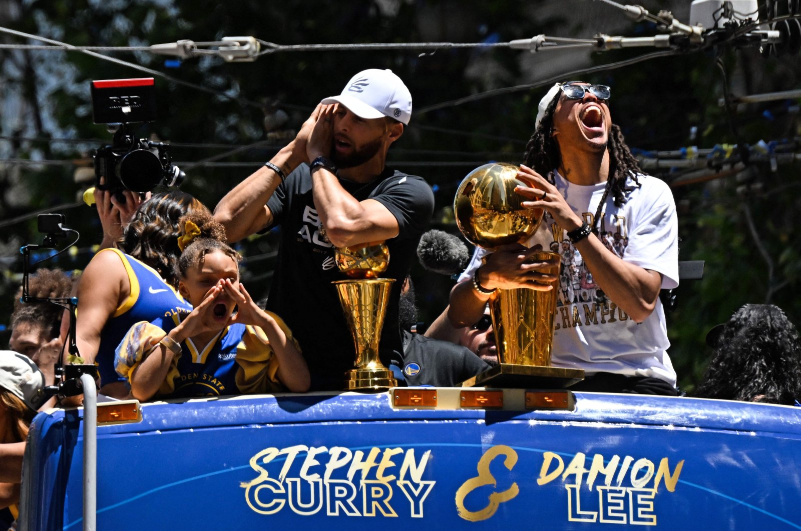 Warriors&#039; Stephen Curry (L) holds the MVP trophy alongside teammate Damion Lee (R) in a victory parade as they celebrate winning the NBA title, San Francisco, California, U.S., June 20, 2022. (AFP Photo)
