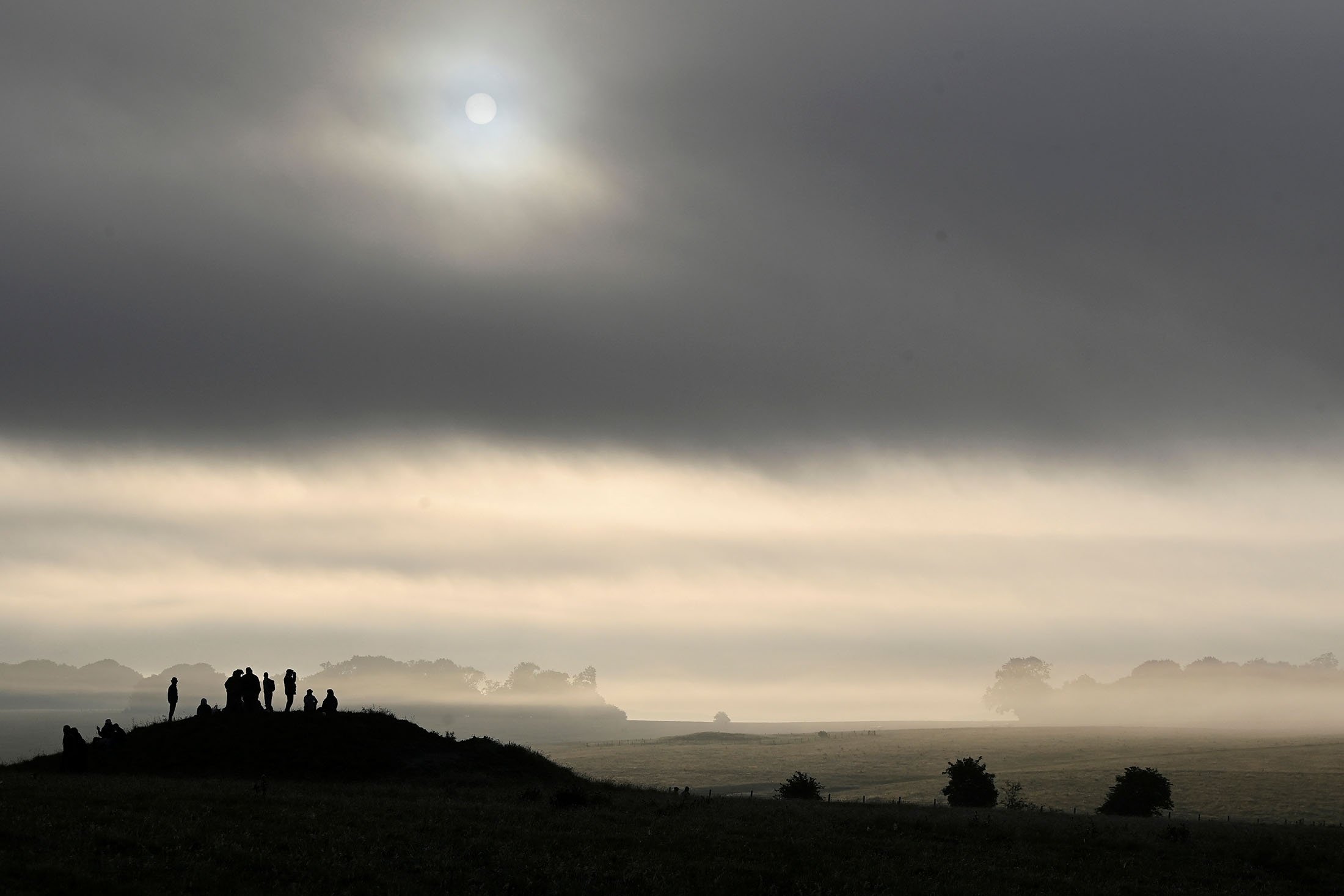 Orang-orang yang bersuka ria berdiri di atas gundukan pemakaman kuno saat mereka merayakan titik balik matahari musim panas di Stonehenge, dekat Amesbury, di Wiltshire, Inggris, 21 Juni 2022. (Foto Reuters)