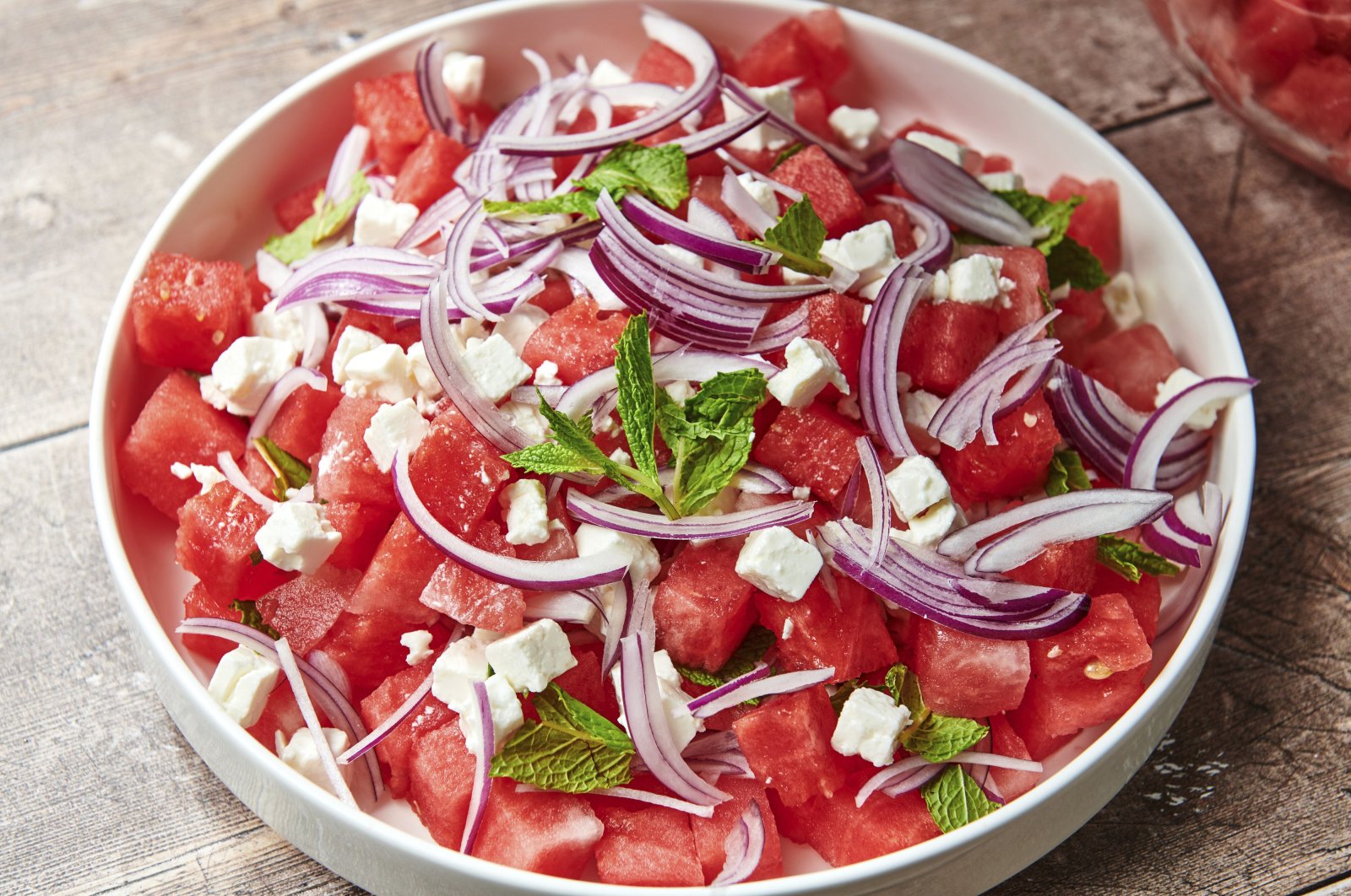 A watermelon feta salad topped with thinly sliced red onion and mint leaves. (AP Photo)