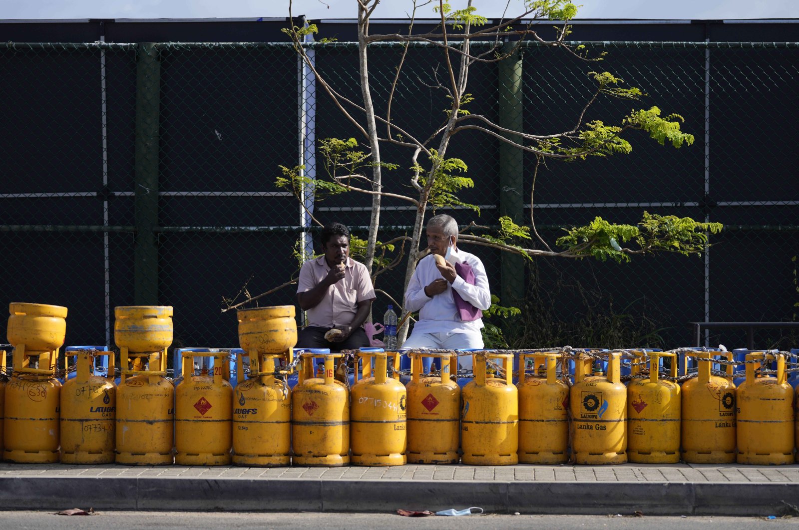People have breakfast while sitting by a line of empty gas canisters that are placed outside the Galle International Cricket Stadium, in Galle, Sri Lanka, June 28, 2022. (AP Photo)