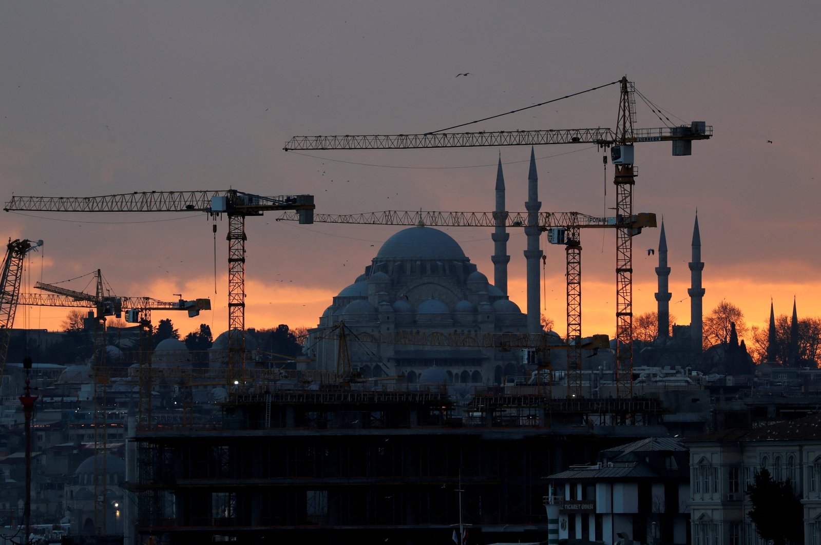 The sun sets behind the cranes of the Galata Port construction site and a mosque in Istanbul, Turkey, Jan. 23, 2020. (Reuters Photo)