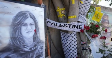 Yellow tape marks bullet holes on a tree and a portrait and flowers create a makeshift memorial on May 19, 2022, at the site where Palestinian-American Al-Jazeera journalist Shireen Abu Akleh was shot and killed, in the occupied West Bank city of Jenin, Palestine. (AP Photo)