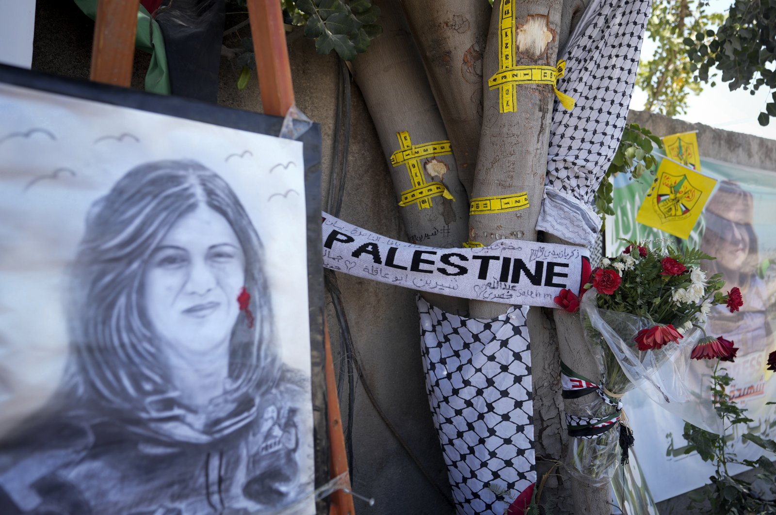 Yellow tape marks bullet holes on a tree and a portrait and flowers create a makeshift memorial on May 19, 2022, at the site where Palestinian-American Al-Jazeera journalist Shireen Abu Akleh was shot and killed, in the occupied West Bank city of Jenin, Palestine. (AP Photo)