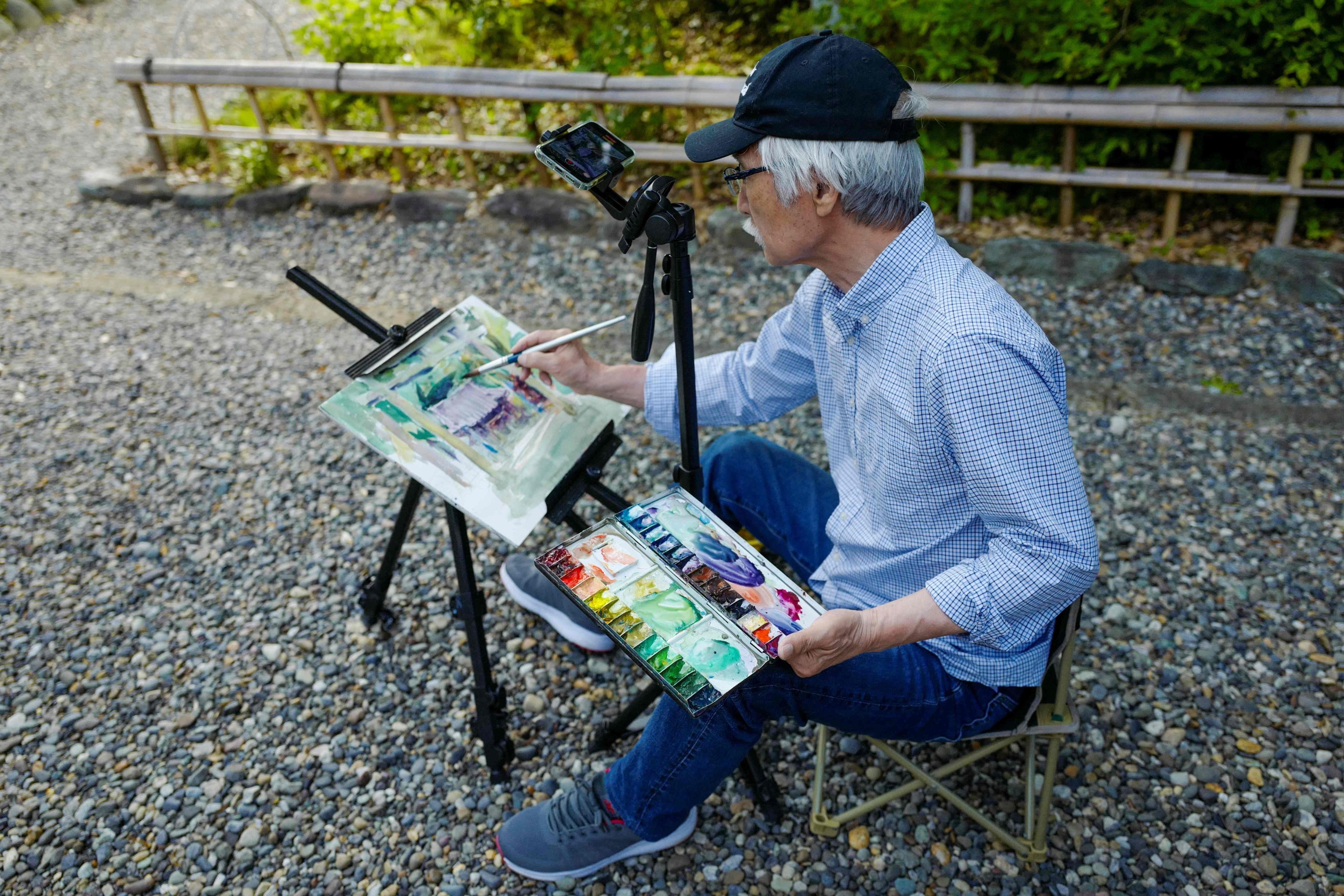 Japanese art instructor Harumichi Shibasaki paints with watercolors while recording video footage using his phone at a shrine in Isumi, Chiba prefecture, Japan, May 25, 2022. (AFP)