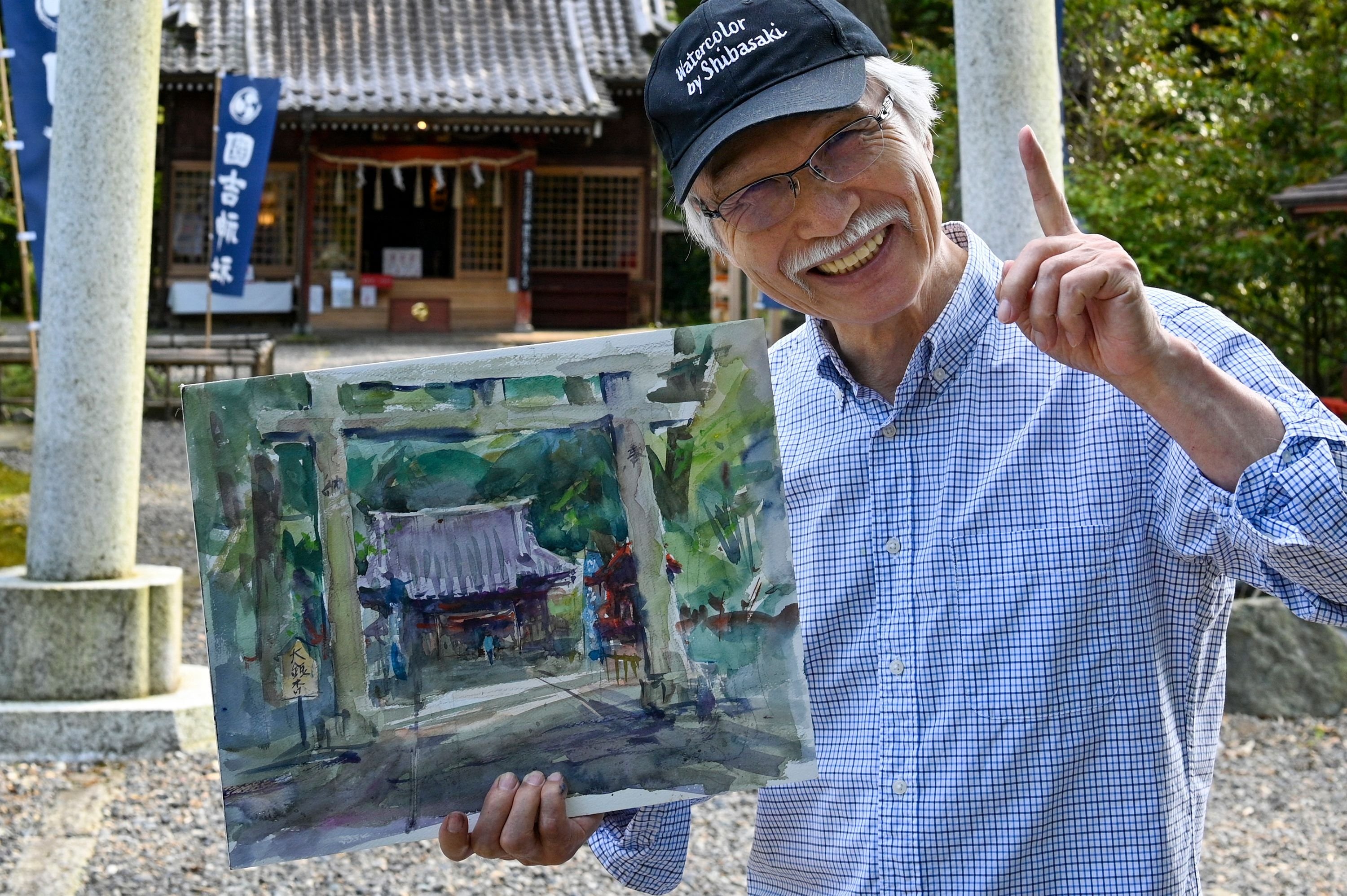 Japanese art instructor Harumichi Shibasaki poses with his finished watercolor painting at a shrine in Isumi, Chiba prefecture, Japan, May 25, 2022. (AFP)