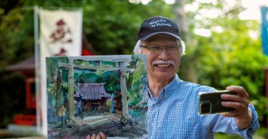 Japanese art instructor Harumichi Shibasaki poses with his finished watercolor painting while holding up his phone at a shrine in Isumi, Chiba prefecture, Japan, May 25, 2022. (AFP)
