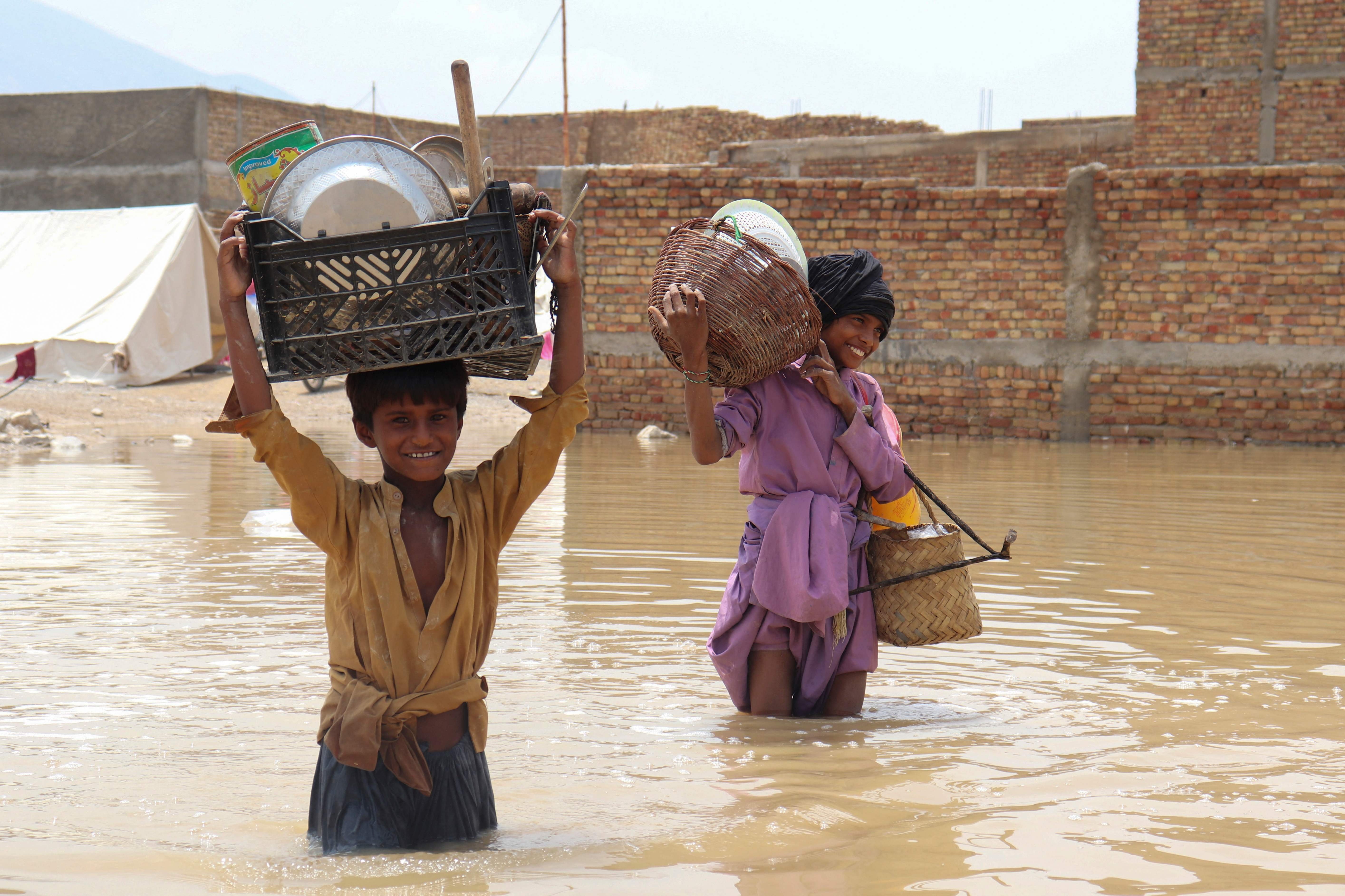 Children carrying household items wade through a flooded area after a monsoon rainfall in Quetta, Pakistan, July 5, 2022. (Photo by Banaras KHAN / AFP)