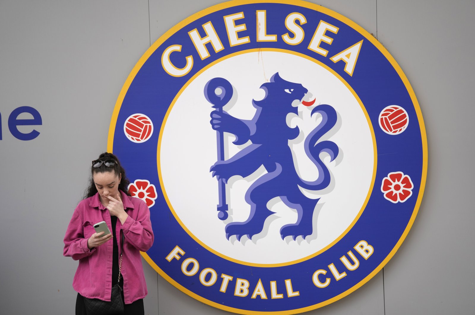 A woman checks her phone outside the Stamford Bridge stadium, London, England, May 7, 2022. (AP Photo)