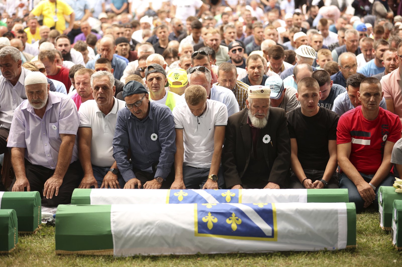 Bosnian muslim men pray next to the coffins containing the remains of 50 newly identified victims of the Srebrenica Genocide, Potocari, Bosnia-Herzegovina, July 11, 2022. (AP Photo)