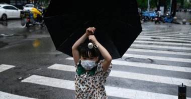 A child holding an umbrella crosses a street in Beijing, China, July 12, 2022. (AFP Photo)