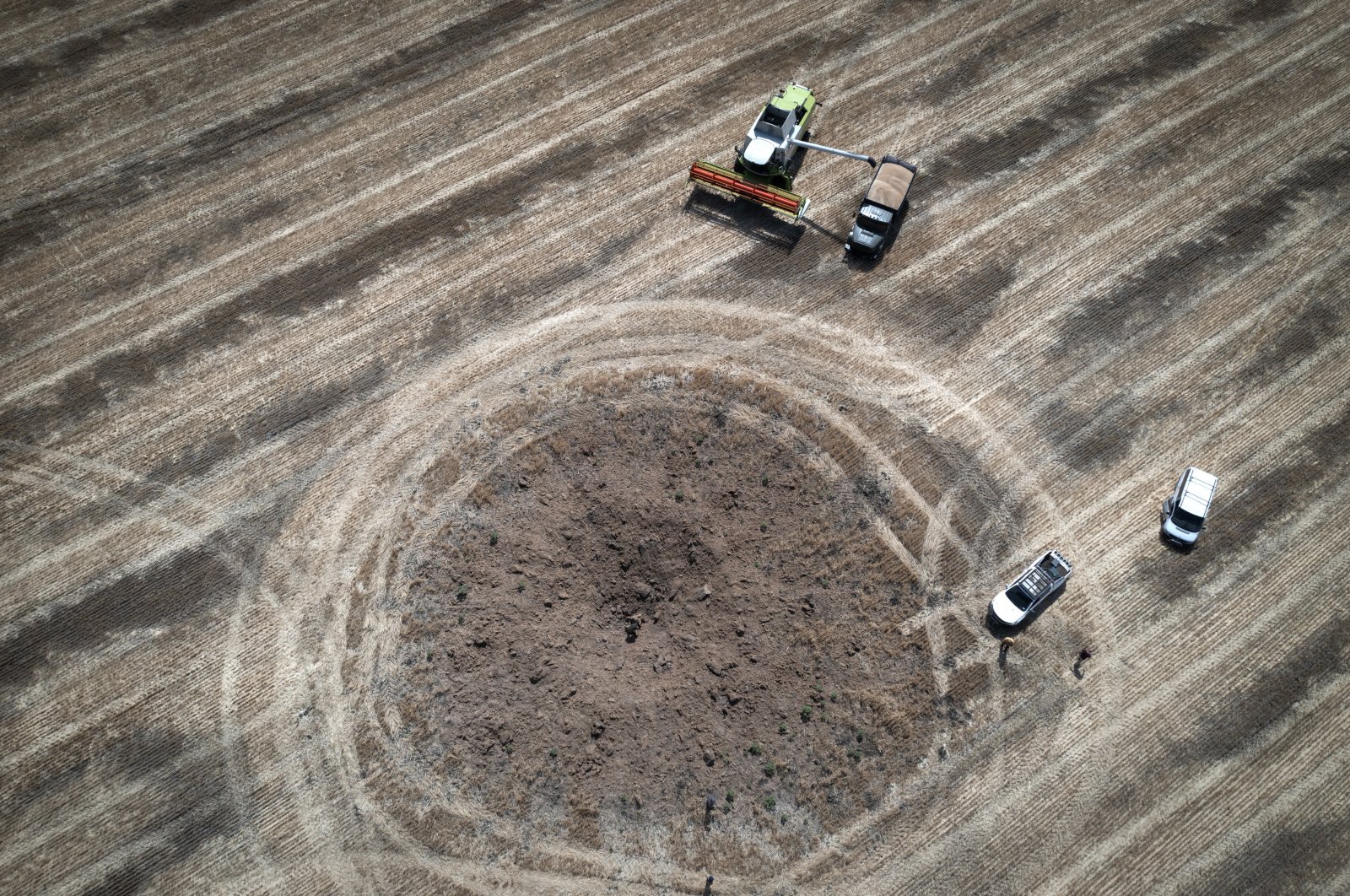 A farmer collects a harvest on a field beside a crater left by a Russian rocket, in the Dnipropetrovsk region, Ukraine, July 4, 2022. (AP Photo)