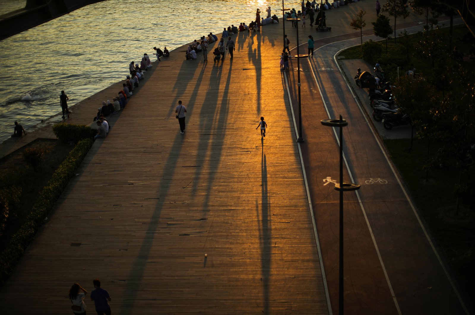 People cast long shadows on the ground as they gather on a promenade next to the Bosporus in Istanbul, Turkey, July 12, 2022. (AP Photo)