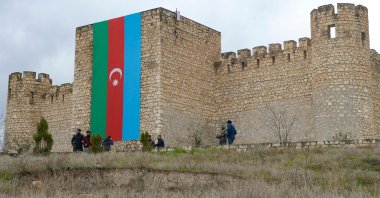 People walk in front of the Azerbaijani flag decorating Shahbulag Castle outside Aghdam, Azerbaijan, March 12, 2022. (AFP Photo)