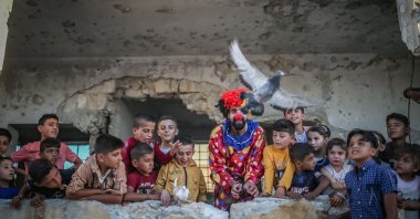 Displaced children and a clown who volunteers to entertain them watch as a pigeon flies in war-hit Idlib, northern Syria, July 11, 2022. (AA Photo)