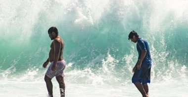 People walk in front of the high surf near Kapahulu Groin (Waikiki Wall) in Waikiki, Hawaii, U.S., July 17, 2022. (Honolulu Star-Advertiser via AP)