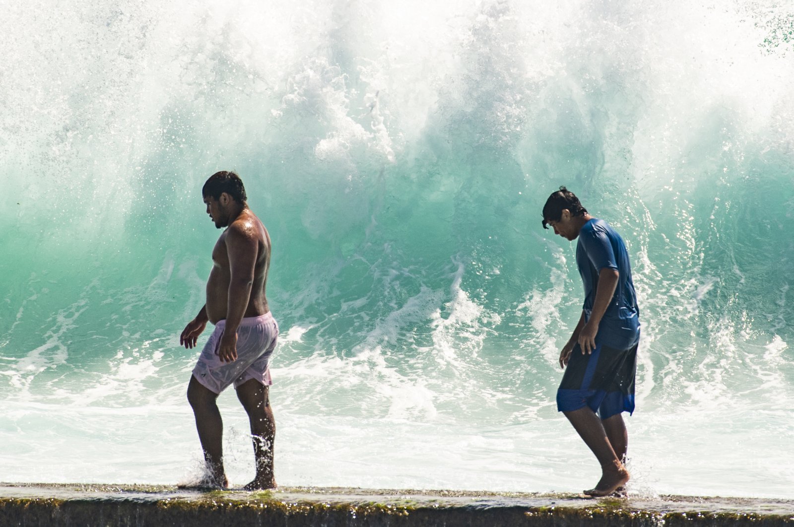 People walk in front of the high surf near Kapahulu Groin (Waikiki Wall) in Waikiki, Hawaii, U.S., July 17, 2022. (Honolulu Star-Advertiser via AP)