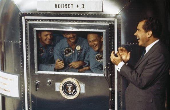 (kiri), Neil Armstrong, Michael Collins dan Edwin 'Buzz' Aldrin Jnr, kru misi pendaratan bulan Apollo 11 yang bersejarah dikenai masa karantina setelah mereka kembali ke bumi.  Melalui jendela Fasilitas Karantina Bergerak mereka, mereka mengadakan percakapan dengan Presiden Richard Nixon, 24 Juli 1969. (Getty Images)