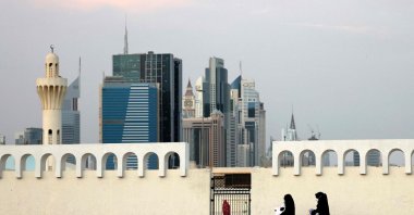 People walk past a gate with Dubai's trademark skyscrapers in the background, on July ,9, 2022. (AFP Photo)