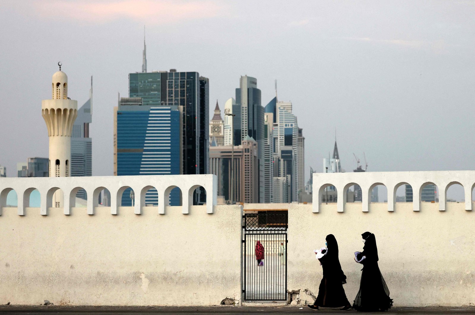 People walk past a gate with Dubai&#039;s trademark skyscrapers in the background, on July ,9, 2022. (AFP Photo)