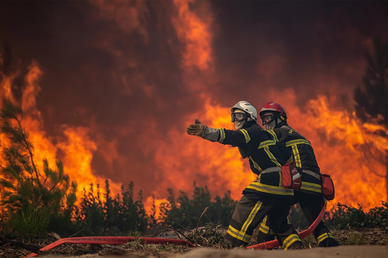 This photo provided by the fire brigade of the Gironde region (SDIS 33) shows firefighters unrolling a fire hose at a forest fire at La Test-de-Buch, southwestern France, July 18, 2022. France scrambled to coordinate more water-bombing planes and hundreds more firefighters to combat spreading wildfires that were being fed Monday by hot swirling winds from a searing heat wave broiling much of Europe. (SDIS 33 via AP)