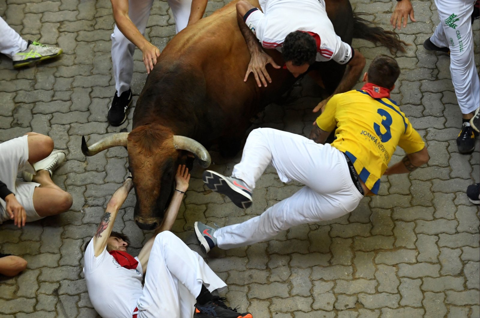 Participants grapple against a Jose Cebada Gago bull during the fifth &quot;encierro&quot; (bull run) of the San Fermin Festival in Pamplona, northern Spain on July 11, 2022. (AFP Photo)