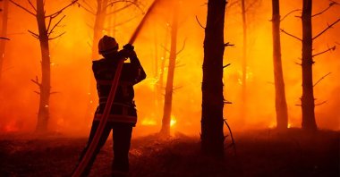 This photo provided by the fire brigade of the Gironde region (SDIS 33) shows a firefighter puts water on a trees at a forest fire at La Test-de-Buch, southwestern France, July 18, 2022. (SDIS 33 via AP)