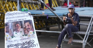 A protester drinks a cup of tea as she sits by a defaced poster carrying portraits of ousted President Gotabaya Rajapaksa (C) and his brothers at the entrance to the president's office in Colombo, Sri Lanka, July 15, 2022. (AP Photo)