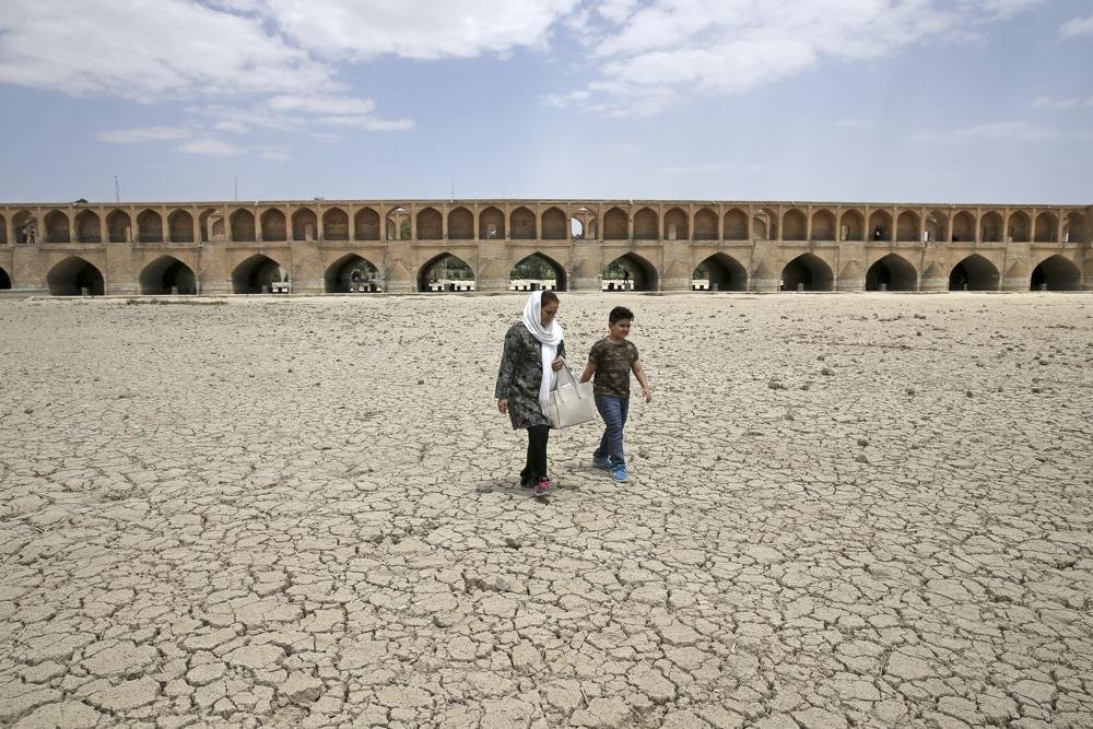A woman and a boy walk on the dried up riverbed of the Zayandeh Roud river that no longer runs under the 400-year-old Si-o-seh Pol bridge, named for its 33 arches, Isfahan, Iran, July 10, 2018. (AP Photo)