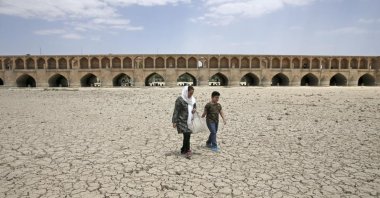 A woman and a boy walk on the dried up riverbed of the Zayandeh Roud river that no longer runs under the 400-year-old Si-o-seh Pol bridge, named for its 33 arches, Isfahan, Iran, July 10, 2018. (AP Photo)