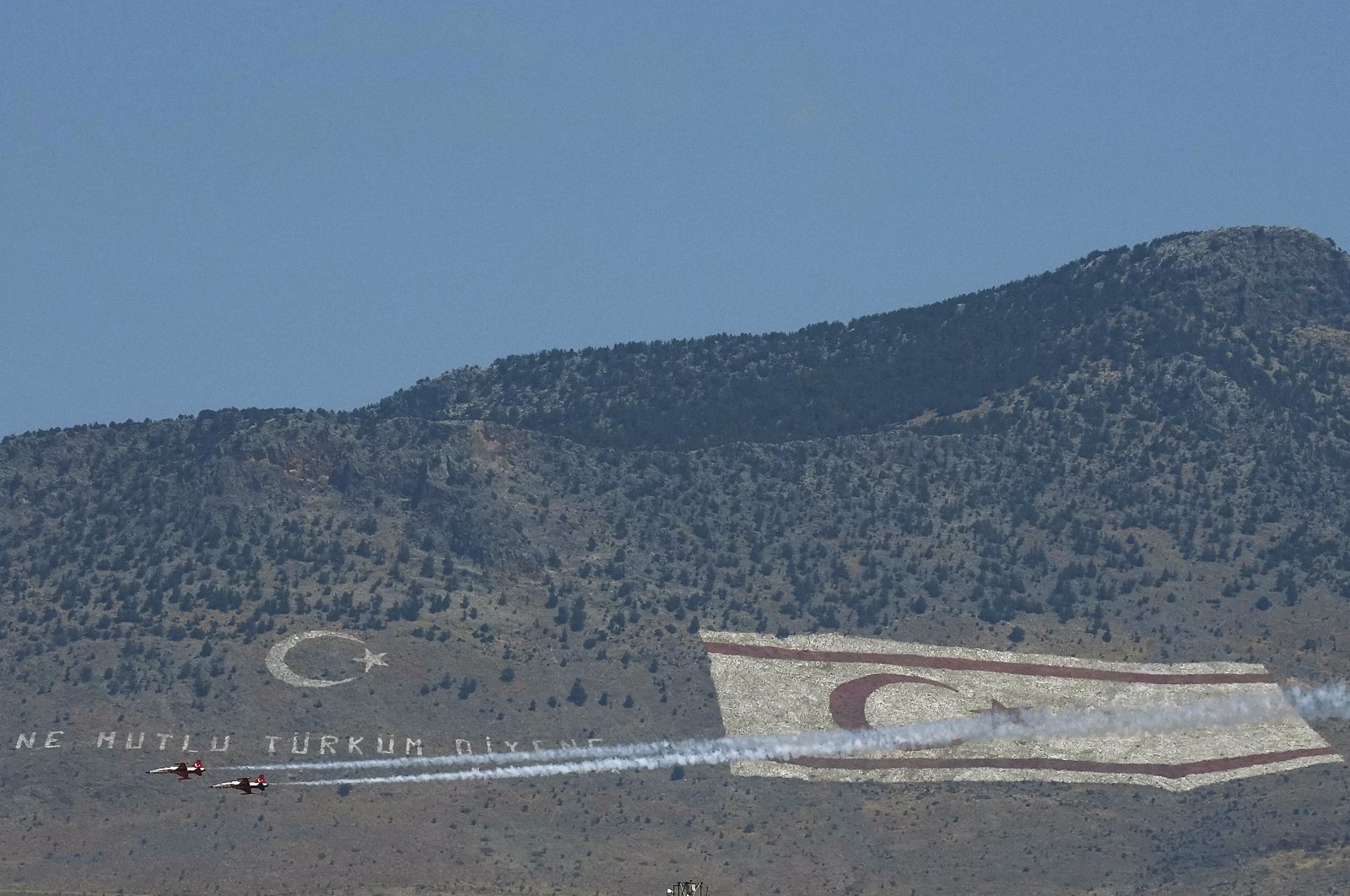 Turkey&#039;s aerobatic aircrafts fly in front of the giant Turkish flag and a Turkish Cypriot flag seen on the Pentadahtilos mountain during a military parade marking the 48th anniversary of the 1974 Turkish operation in the Turkish area of the divided capital Nicosia, Cyprus, July 20, 2022. (AP Photo)