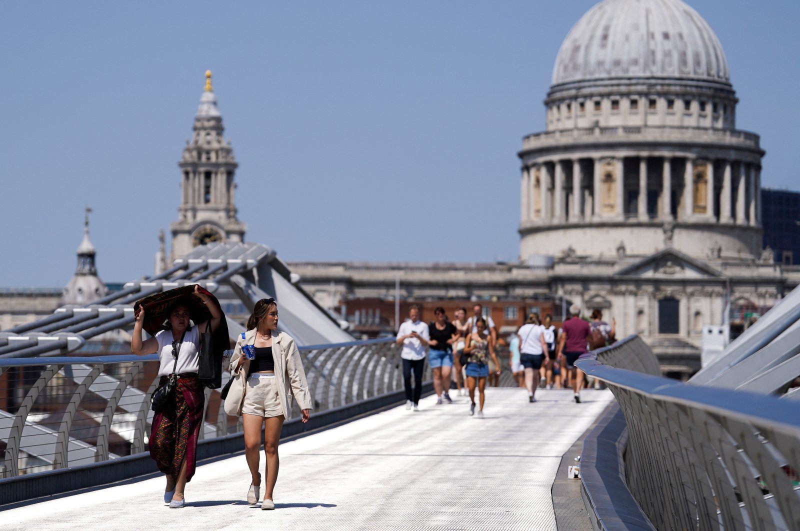 People cover themselves from the sun at Millennium Bridge during a heatwave, in London, U.K., July 18, 2022. (Reuters Photo)