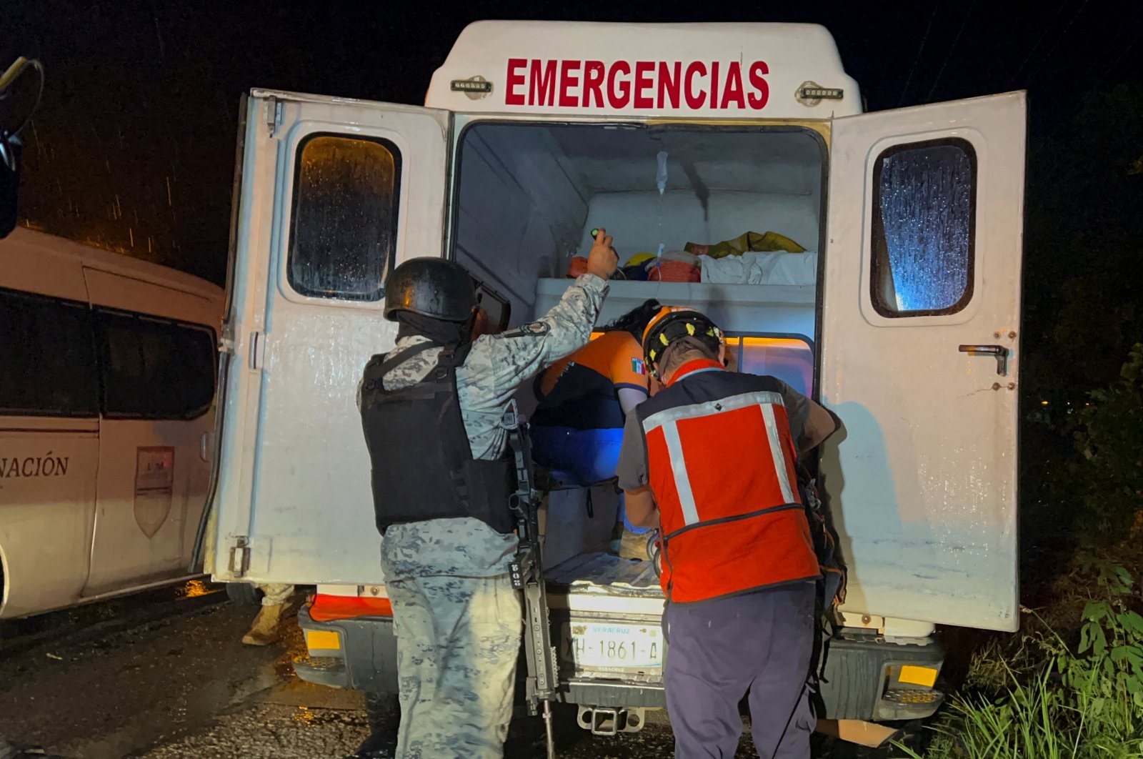 A member of the National Guard uses a torch to help a paramedic giving first aid to a migrant injured inside an ambulance, in the town of Acayucan, in Veracruz state, Mexico, July 27, 2022. (Reuters Photo)