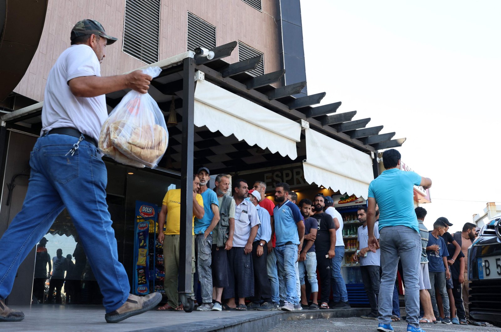 A man walks out of a bakery with a bag of subsidized flatbread, as others continue to wait in a queue, in the capital Beirut, Lebanon, July 29, 2022. (AFP Photo)