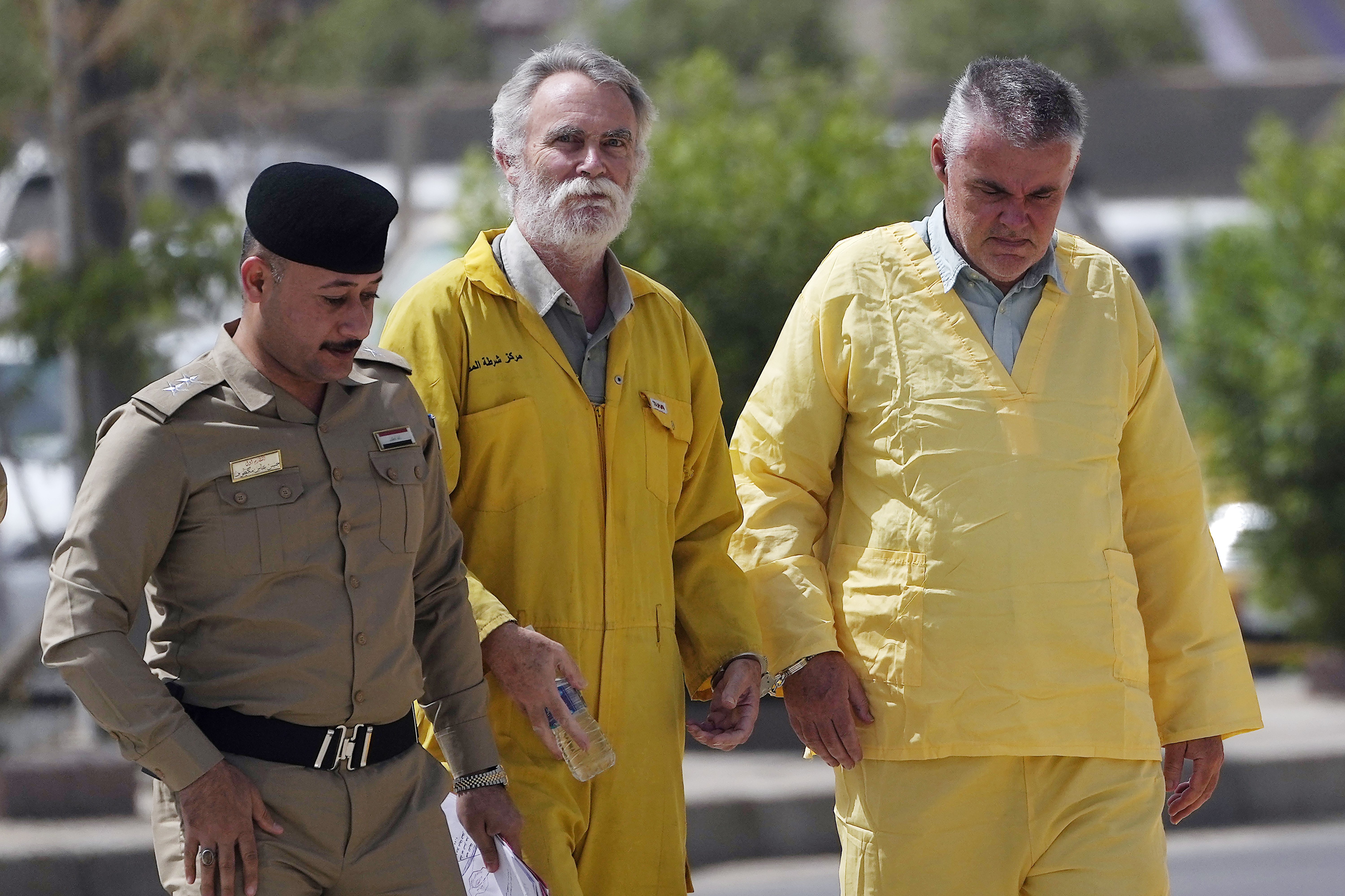 Volker Waldmann (R) and Jim Fitton (C) are handcuffed as they walk to a courtroom escorted by police arriving to court in Baghdad, Iraq, May 22, 2022. (AP Photo)