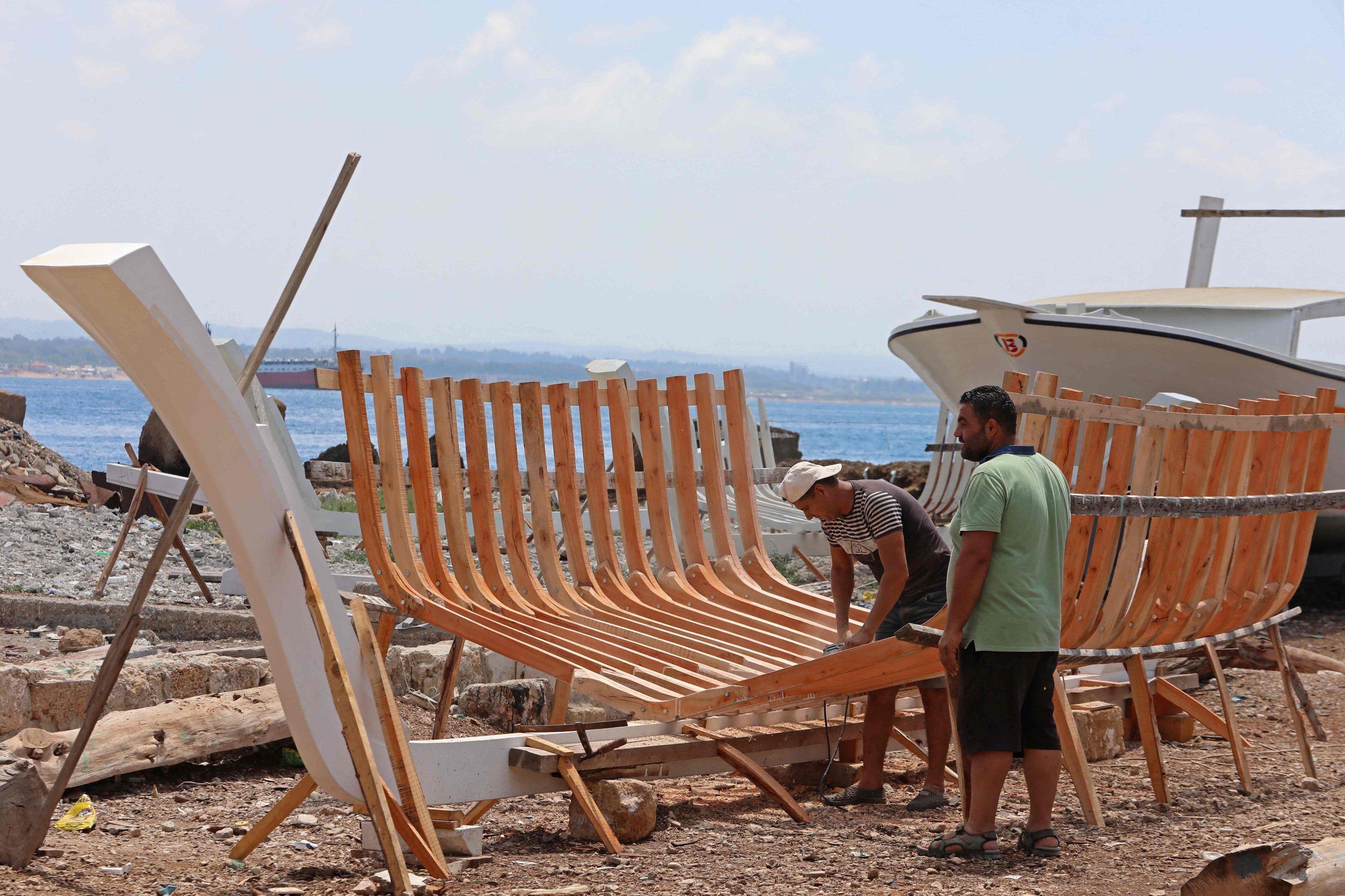 Pengrajin Suriah Khaled Bahlawan (kanan) membuat perahu kayu di galangan kapalnya di Pulau Arwad, Mediterania, Suriah pada 24 Juli 2022. (AFP)
