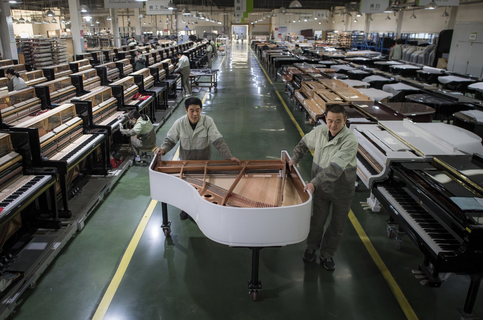 Workers transfer a half-assembled piano at a production factory of Parsons Music Corporation in Yichang, Hubei province, China, Nov. 23, 2021. (Xinhua via AP )