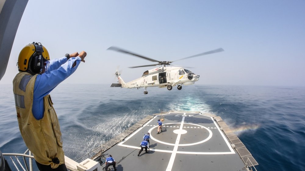 Helicopter deck officer give hand signal to Sikorsky S-70 Sea Hawk helicopter hovering above helicopter deck of Thai Navy ship to receive supplies, Chonburi, Thailand, Jan. 29, 2014. (Shutterstock Photo) 