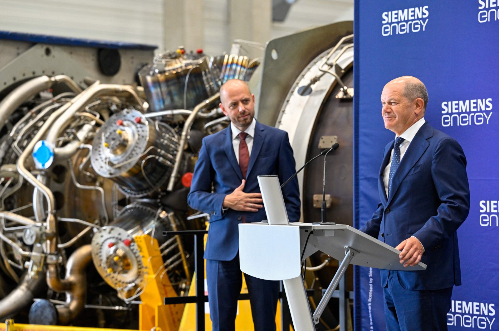 German Chancellor Olaf Scholz (R) stands next to Christian Bruch, President and CEO of Siemens Energy, in front of a turbine of the Nord Stream 1 pipeline as Scholz gives a statement during a visit at the plant of Siemens Energy in Muelheim an der Ruhr, western Germany, Aug. 3, 2022. (AFP Photo)
