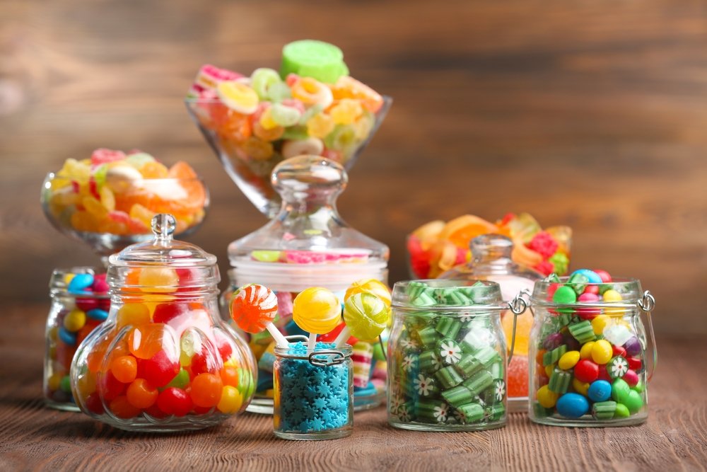Colorful candies in jars on table on wooden background. (Shutterstock Photo)