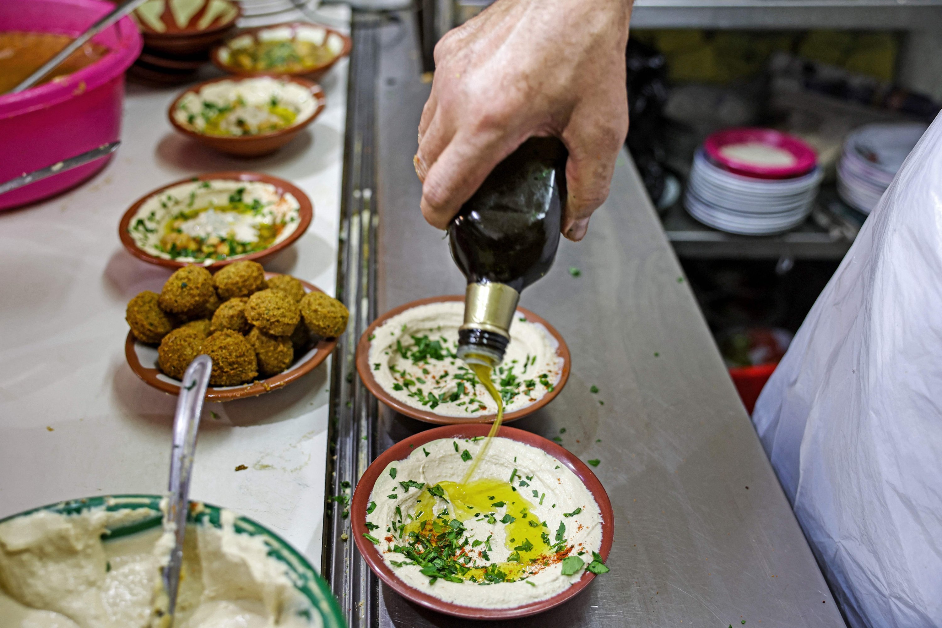 Seorang juru masak menyiapkan sepiring hummus untuk disajikan kepada klien di sebuah restoran di Kota Tua Yerusalem, Palestina yang diduduki, 26 Juli 2022. (AFP Photo)