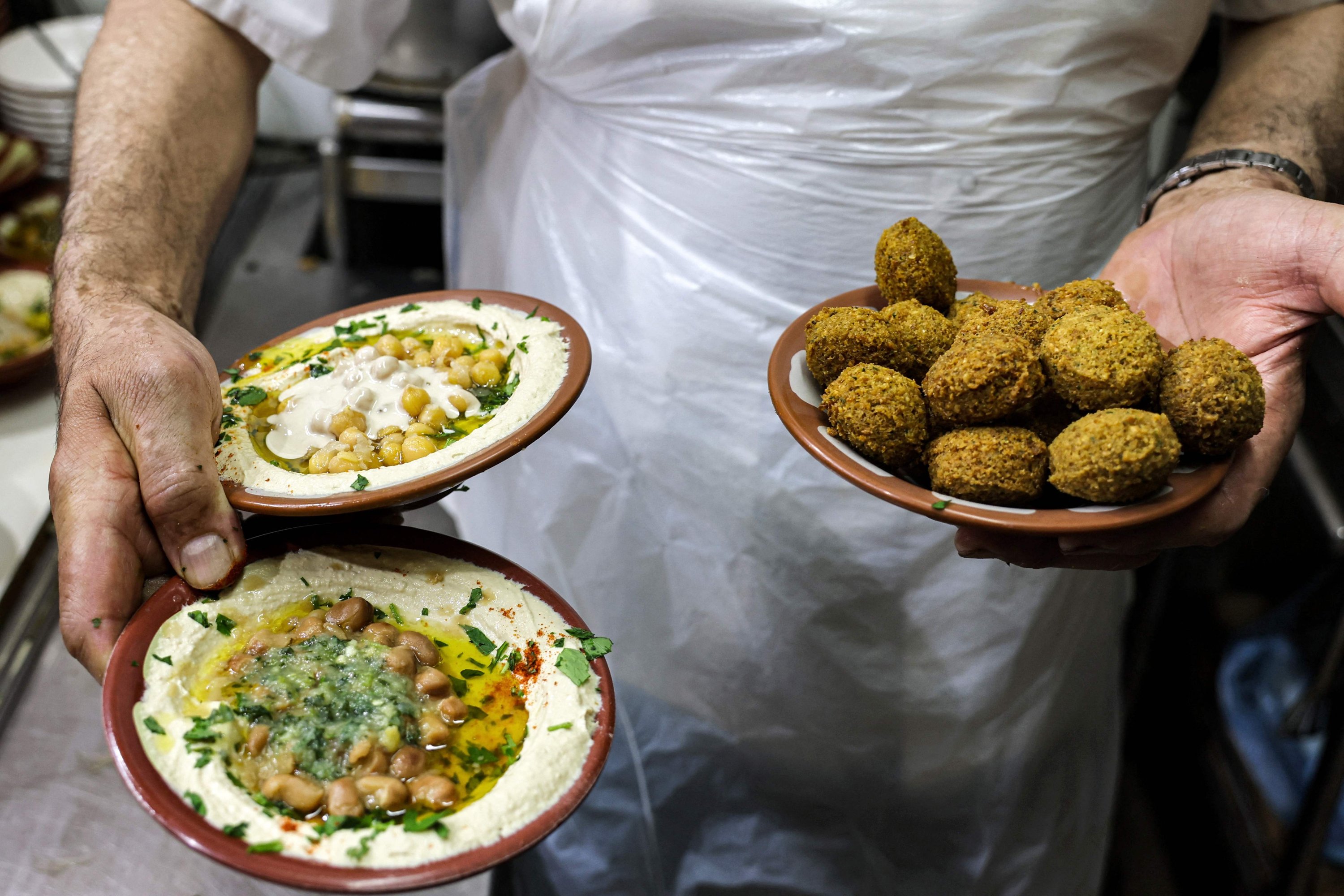 Seorang juru masak bersiap untuk menyajikan sepiring hummus, kacang fava, dan falafel untuk disajikan kepada klien di sebuah restoran di Kota Tua Yerusalem, Palestina yang diduduki, 26 Juli 2022. (AFP Photo)