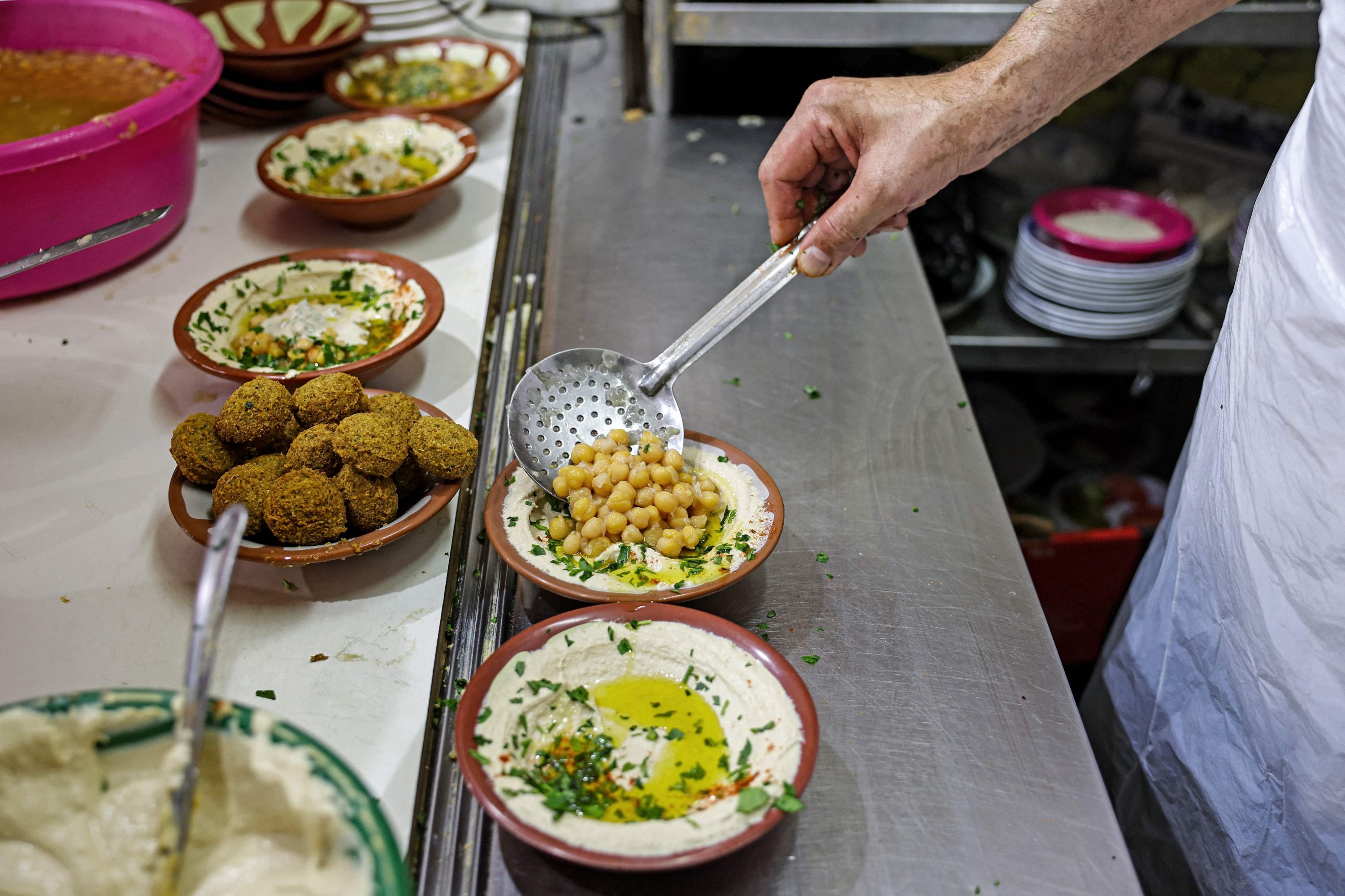 Seorang juru masak menyiapkan sepiring hummus untuk disajikan kepada klien di sebuah restoran di Kota Tua Yerusalem, Palestina yang diduduki, 26 Juli 2022. (AFP Photo)
