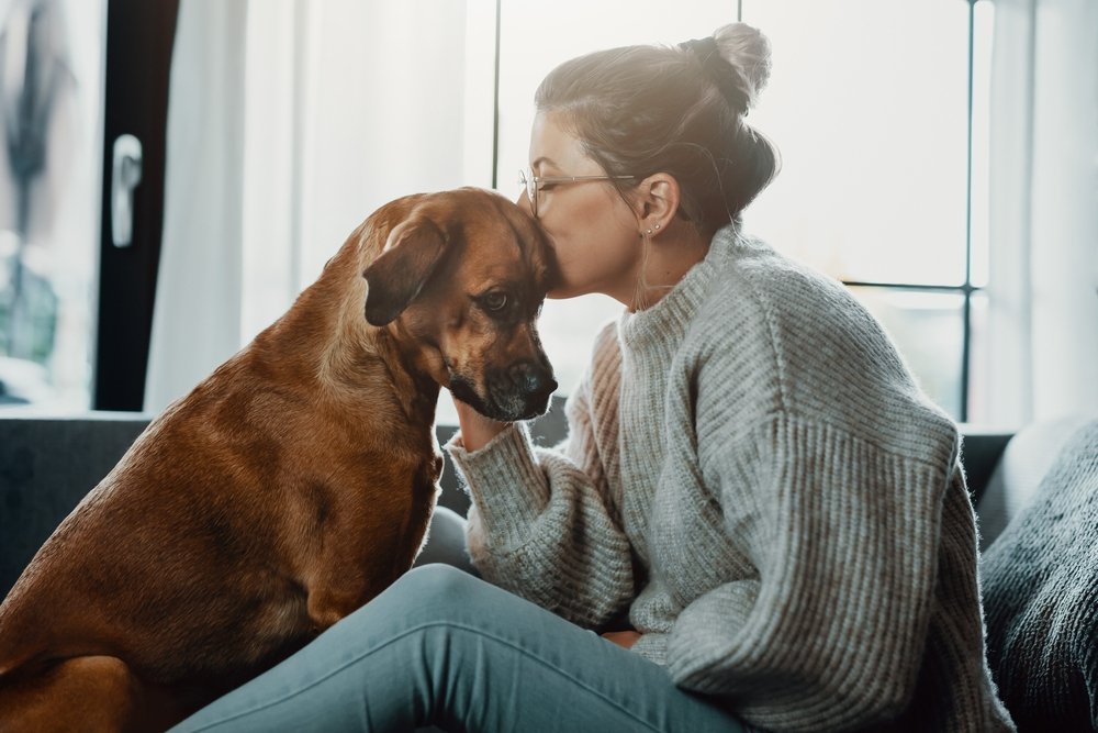 Woman cuddles, plays with her dog at home. (Shutterstock Photo)