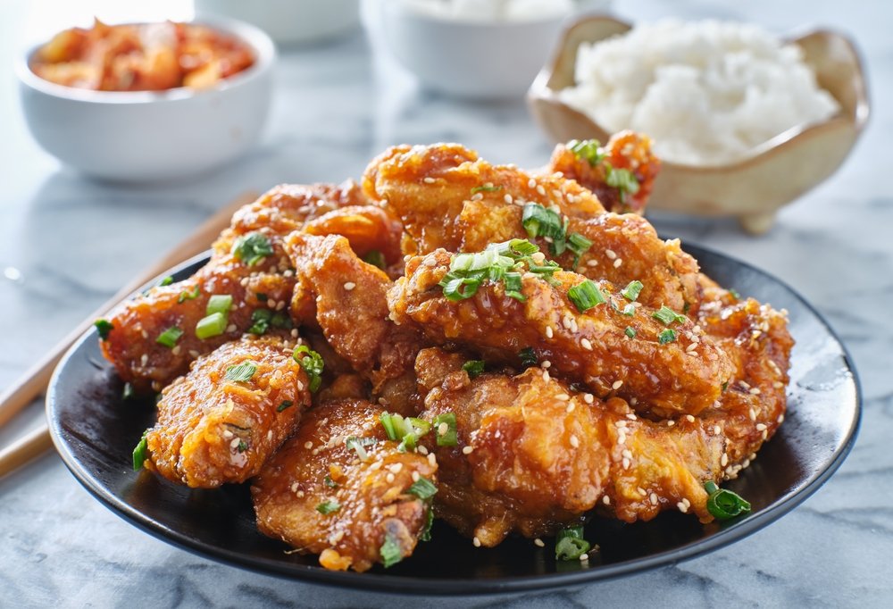 Crispy fried Korean chicken wings in galbi sauce with pickled radish, kimchi, and rice side dishes. (Shutterstock Photo)