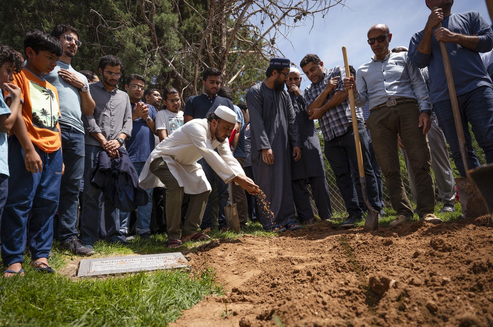 People sprinkle dirt over the grave of Muhammad Afzaal Hussain, 27, at Fairview Memorial Park in Albuquerque, New Mexico, U.S., Aug. 5, 2022. (Chancey Bush/The Albuquerque Journal via AP)