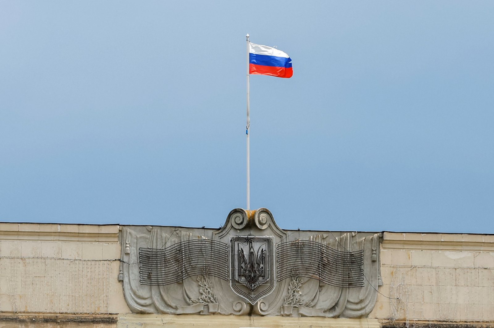 A Russian flag flies above the Ukrainian coat of arms dismantled from a former regional council&#039;s building during the Ukraine-Russia conflict in the Russia-controlled city of Kherson, Ukraine, July 25, 2022. (Reuters Photo)