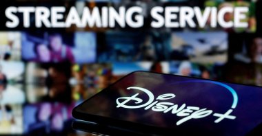 A smartphone screen showing the "Disney " logo is seen in front of the words "streaming service," March 24, 2020. (Reuters Photo)