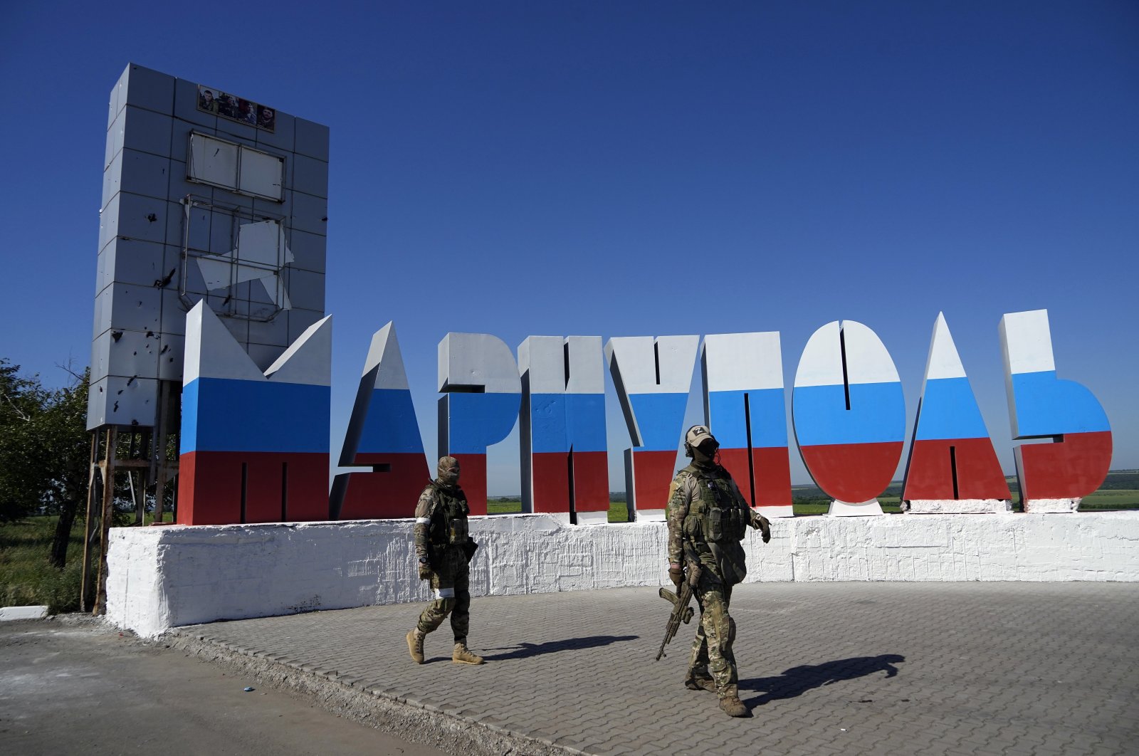 Russian soldiers walk past a repainted city name in the colors of the Russian flag at the entrance of Mariupol, on the territory which is under the Government of the Donetsk People&#039;s Republic control, eastern Ukraine, June 12, 2022. (AP Photo)