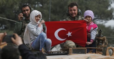 Turkish soldiers atop a tank pose for pictures with Syrian children holding a Turkish flag, during a Turkish government-organized media tour, in the northwestern city of Afrin, Syria. (AP Photo)